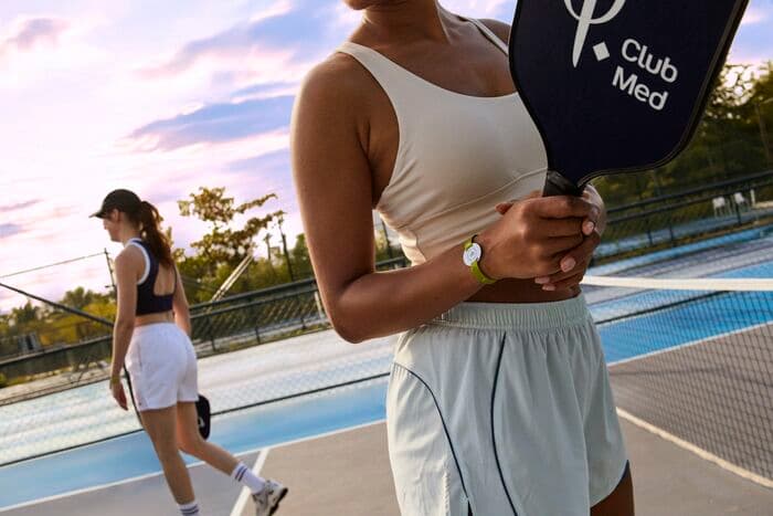 A player holding a Club Med paddle on the pickleball courts at sunset